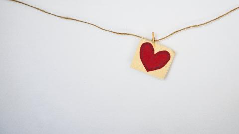 White wall with a piece of material with a heart painted on hanging from a string