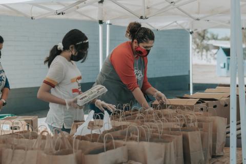 Two volunteers help sort food into paper bags