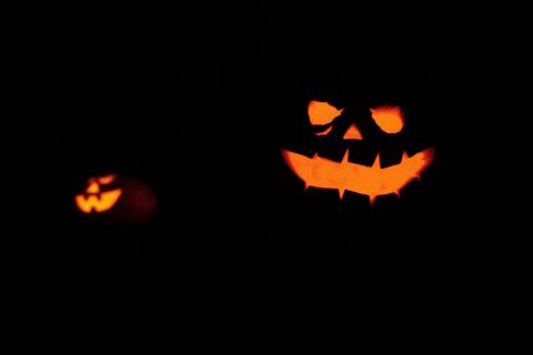 Two halloween pumpkins with faces illuminated in the dark