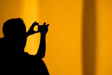 Black silhouette of a person against a yellow background taking a photograph