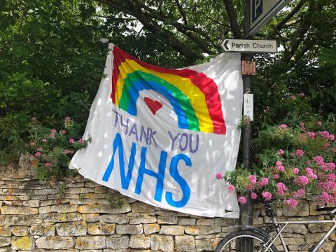 Picture of colourful banner saying 'Thank you NHS' hung up in a tree by a brick fence