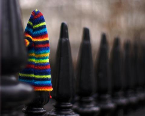 One colourful hat standing out on top of a plain black railing