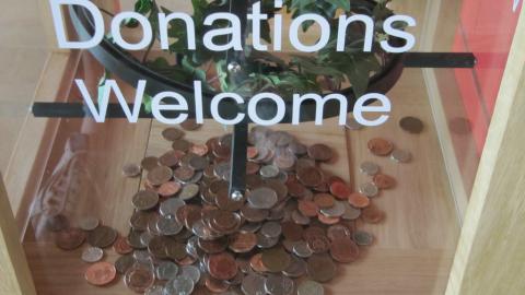 Image of charity donation box with some money in it and a 'donations welcome' sign