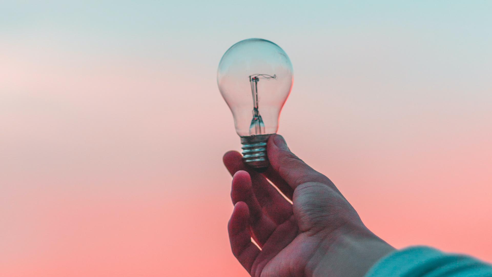 A lightbulb in someone's hand against a blue and pink sky