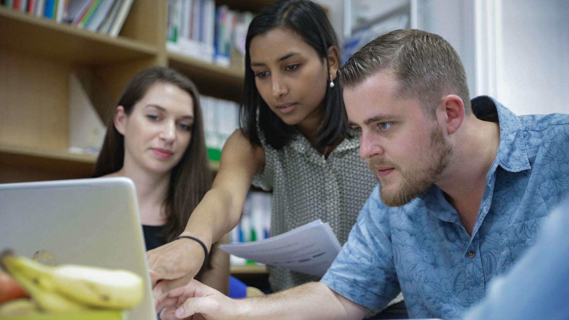 Three office workers look at a computer screen