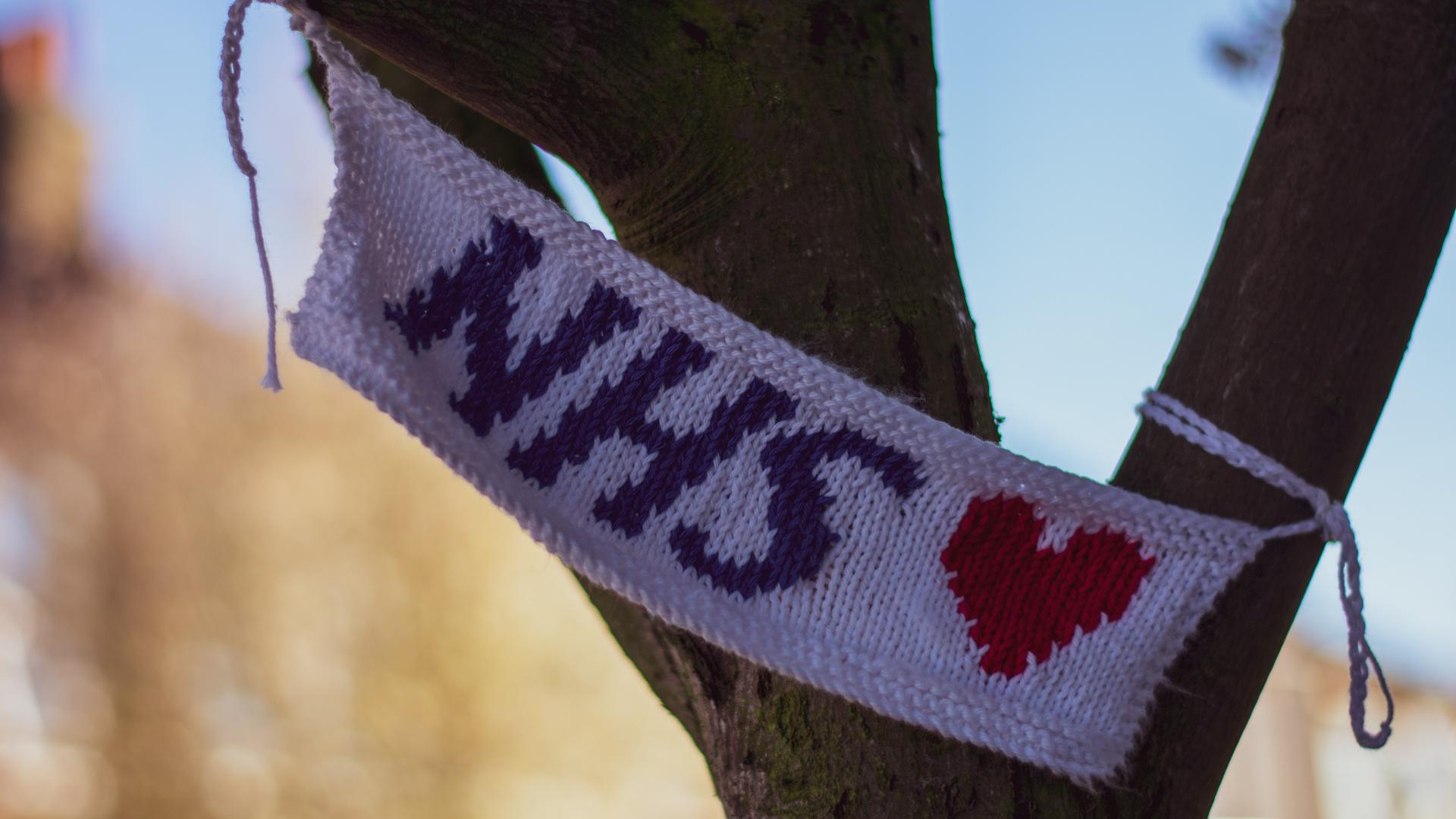 Knitted banner in white, with NHS in blue text and a red heart hanging in a tree