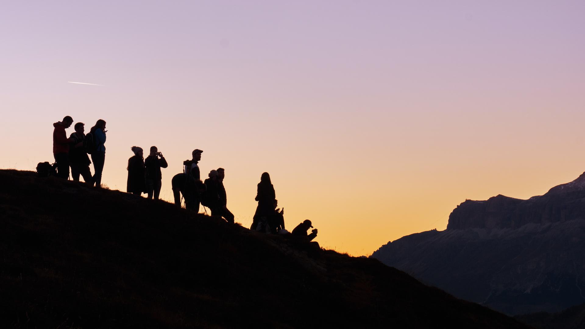 A group of people on a hill silhouetted against the setting sun