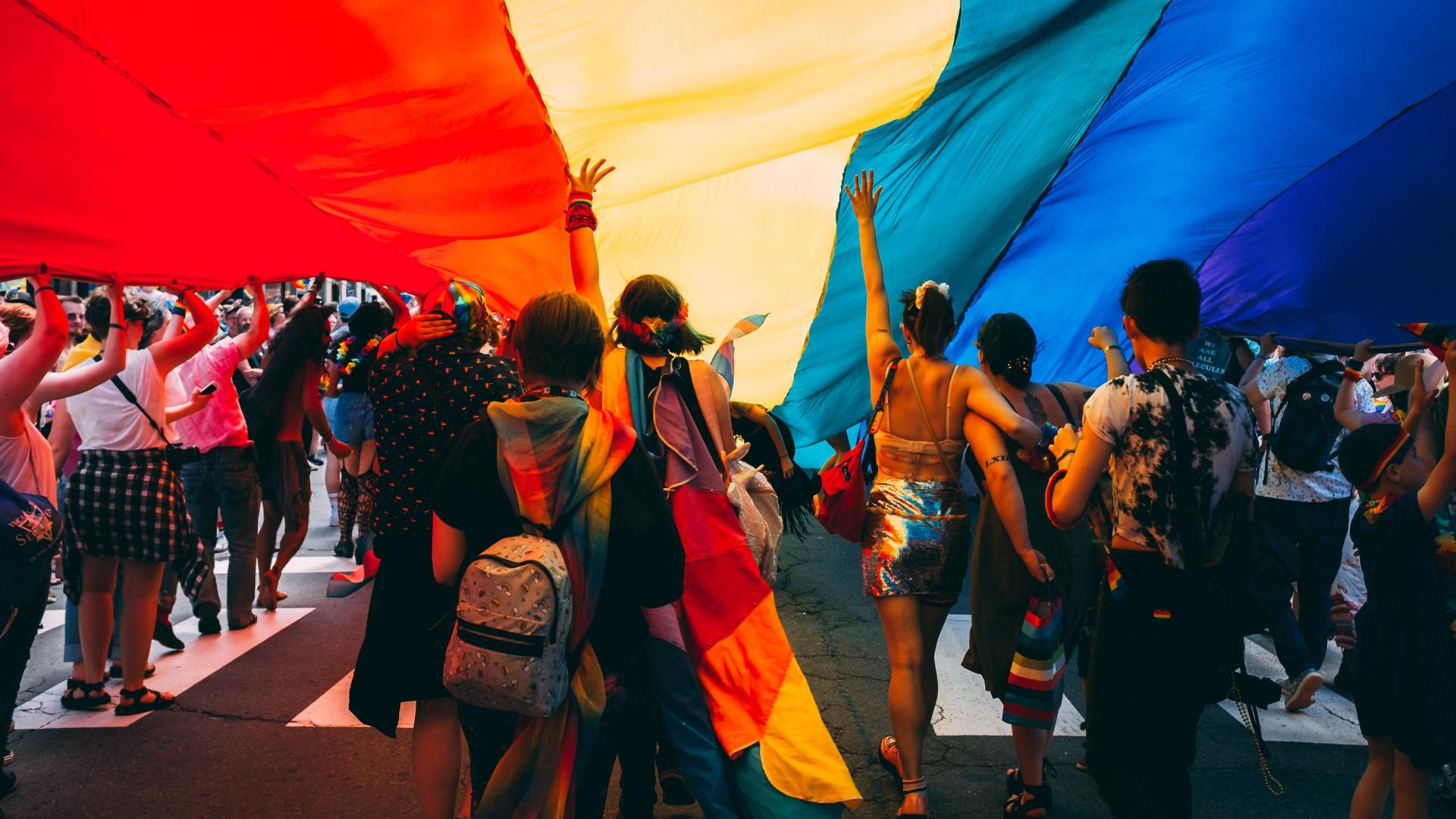 people gathered underneath a rainbow banner