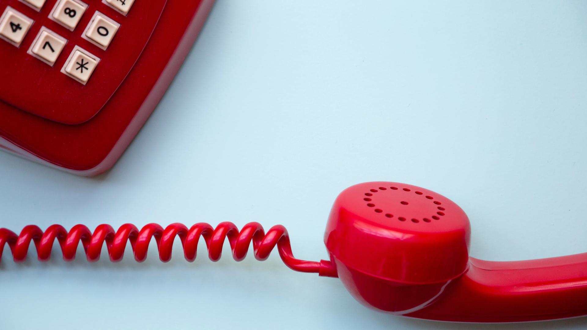 An old style red telephone against a blue background