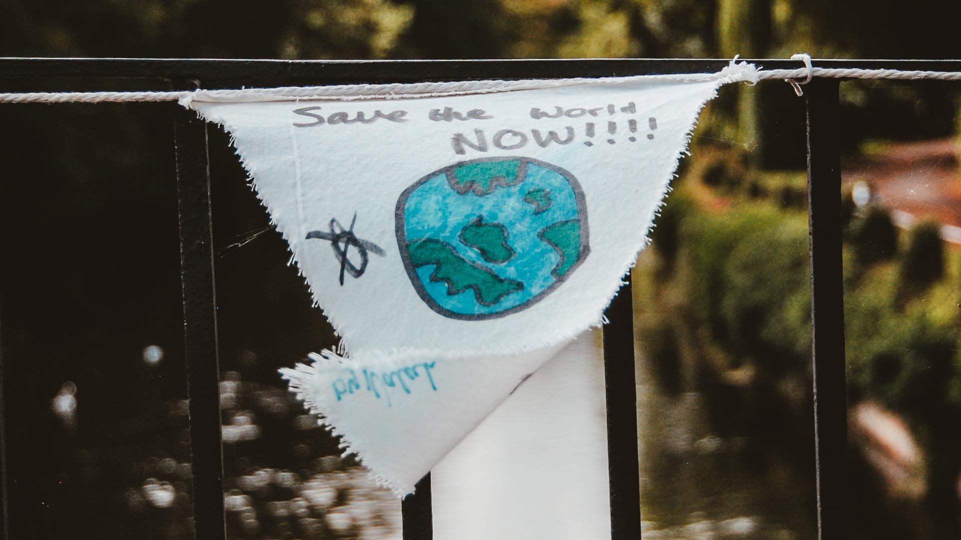 flag tied to a metal gate that has an earth painted on it and says save the world now
