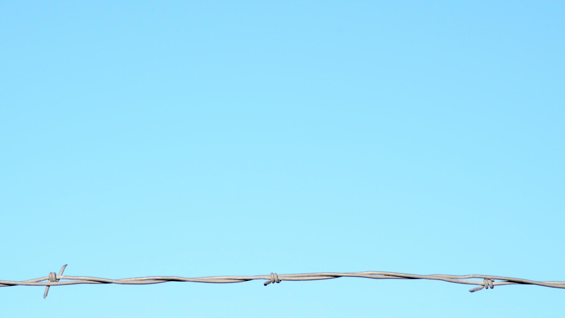 Single line of barbed wire against clear blue sky background