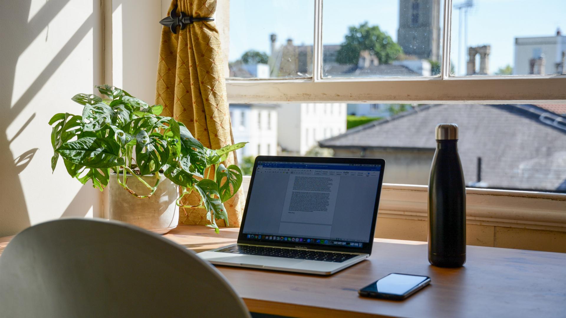 A desk with a laptop on, in front of a sunny window