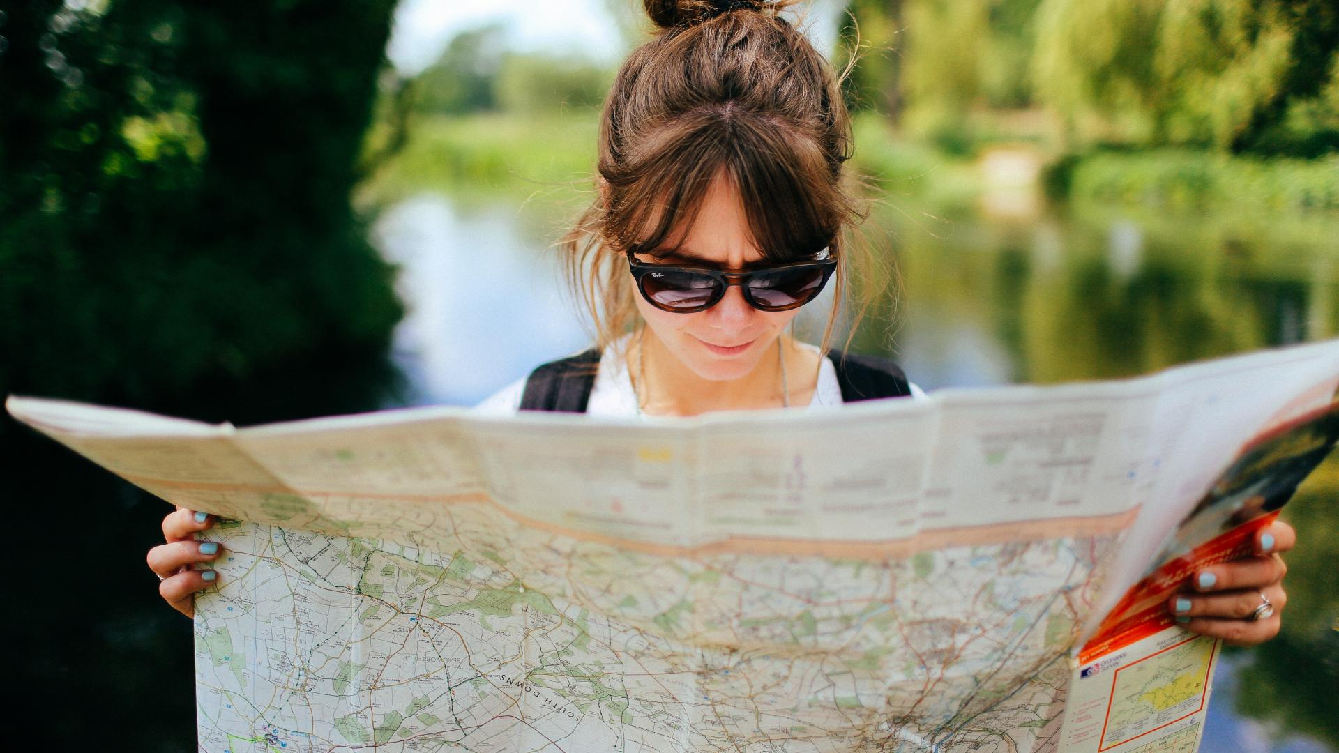 White woman wearing sunglasses looks at a map on a sunny day